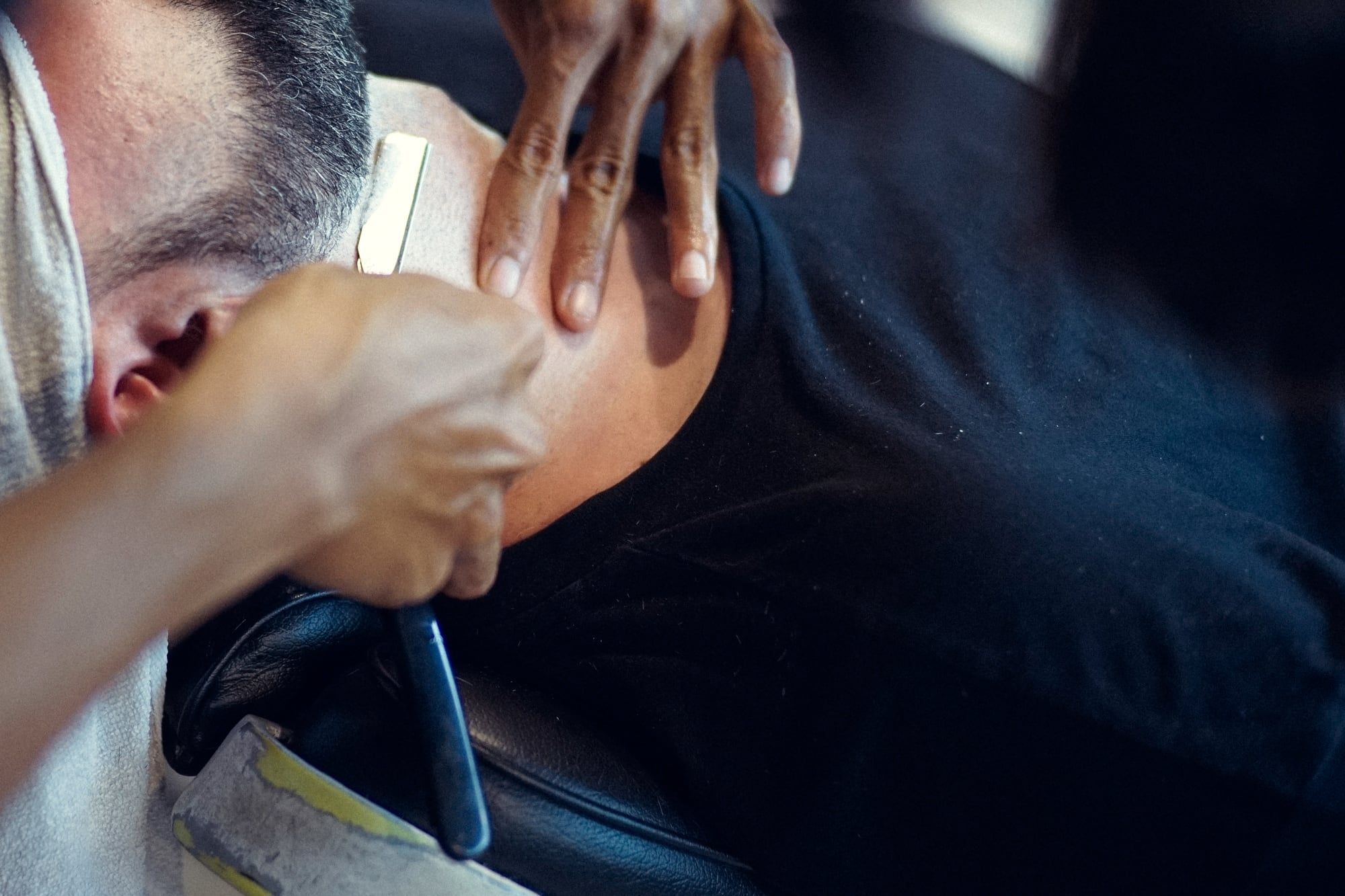 Barbeiro fazendo a barba com navalha e toalha sobre o ombro do cliente