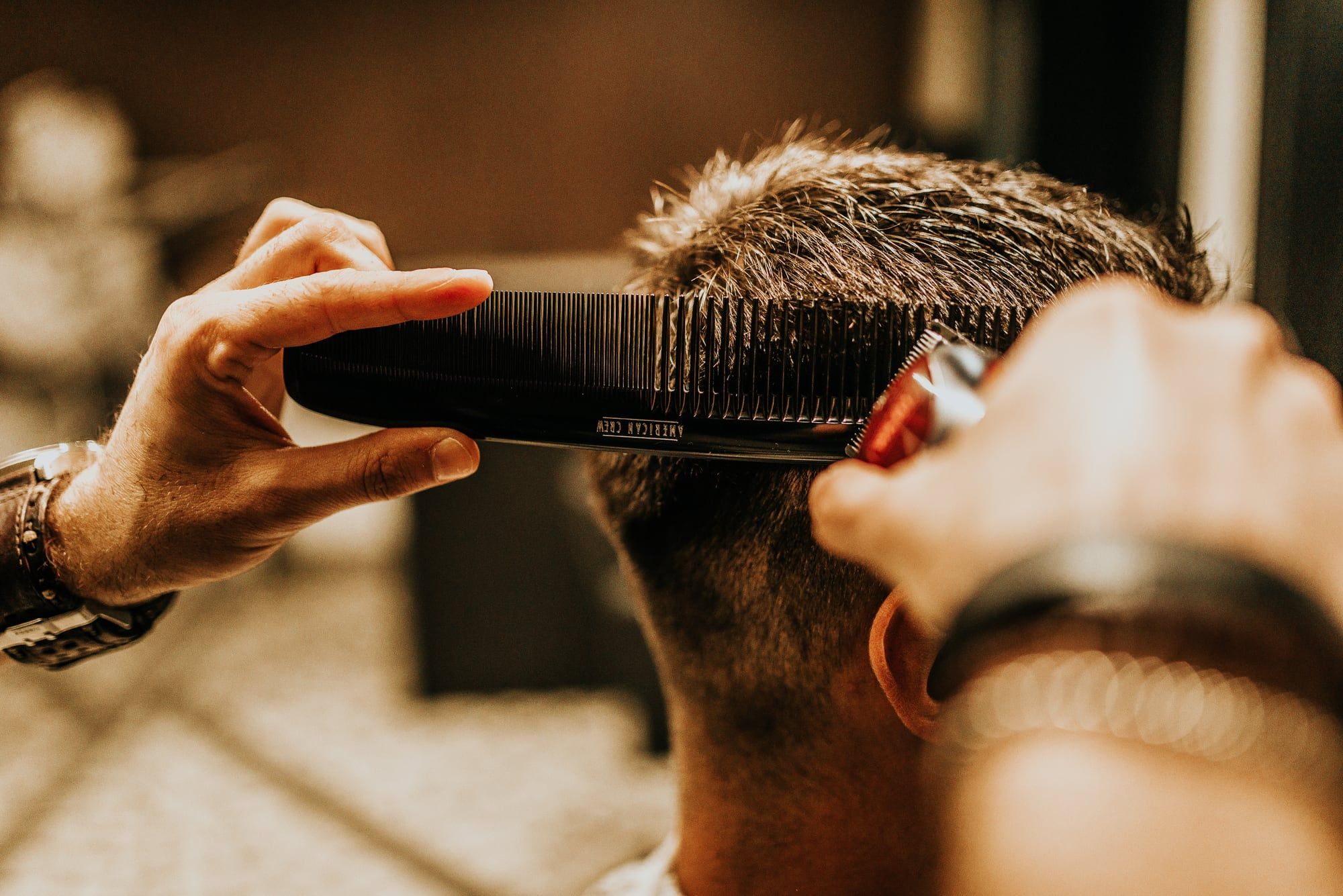 Mãos do barbeiro com pente e máquina aparando a lateral do cabelo
